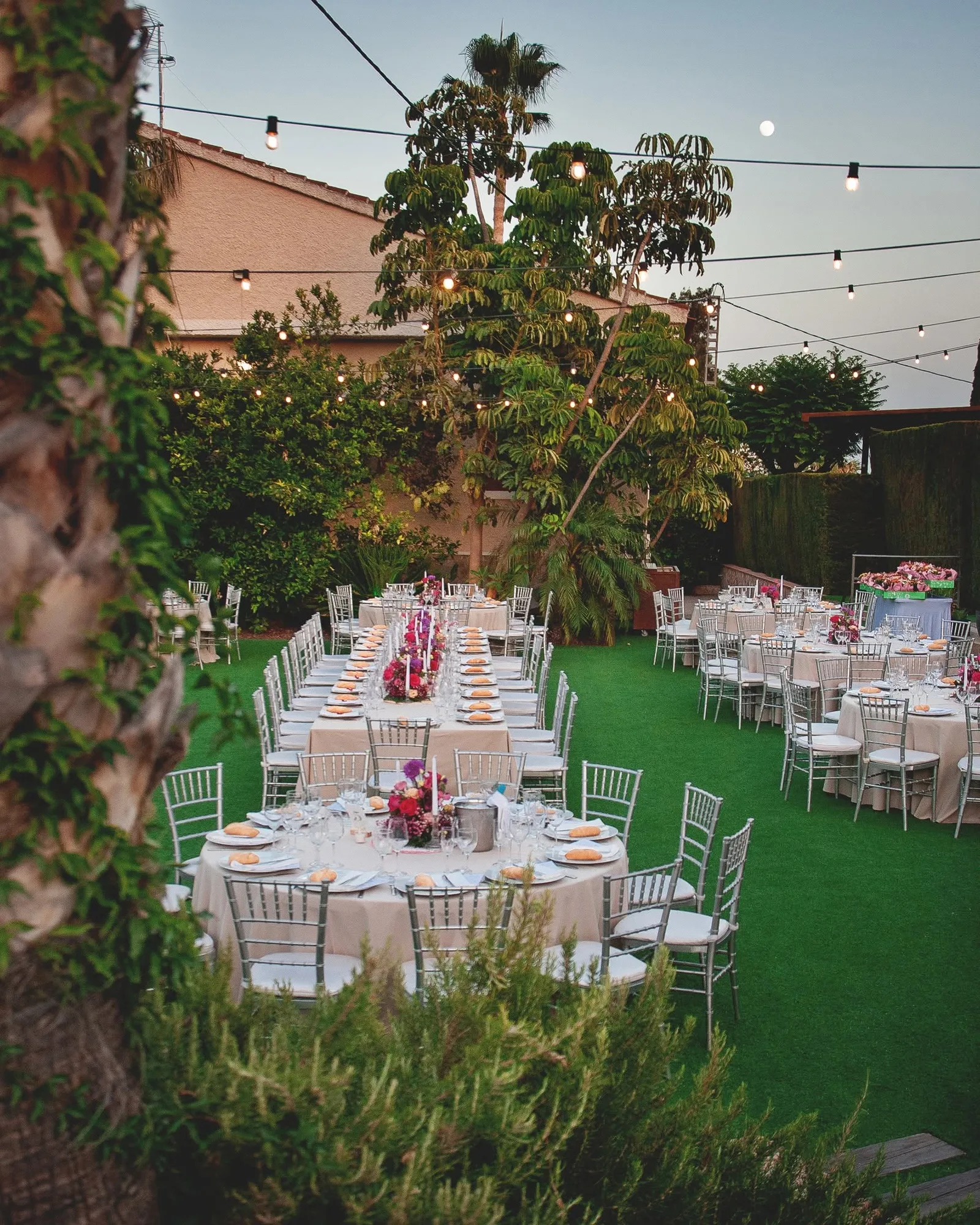 El jardín del restaurante al anochecer, con las mesas vestidas y las guirnaldas de bombillas encendidas
