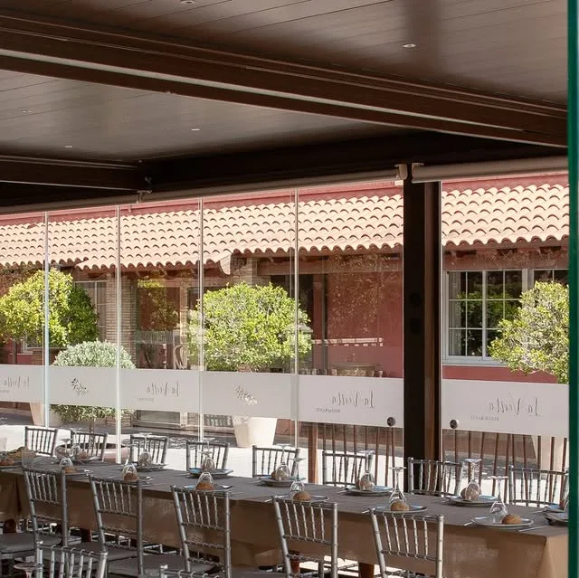 La Pecera: comedor acristalado con mesas largas vestidas y el patio al otro lado del cristal